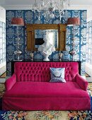 Spacious deep pink couch in luxurious room; wallpaper with large pattern, crystal chandelier and silk rug with large floral pattern