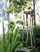 Gartenskulptur auf einem Podest aus Baumstämmen an Hausecke im sonnigen Garten