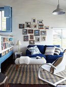 Cheerful blue and white living room below sloping ceiling; collection of photos in vintage picture frames above couch
