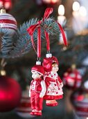 Little boy and girl Christmas tree baubles hung from branch with red ribbon