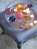 Baubles and lit tealights in glass dish on upholstered Rococo footstool