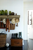 Vintage mudroom with Wellington boots on an old wooden chest and collection of bottles on a wall coat rack
