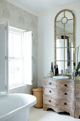 Bathroom with latticed mirror on shabby-chic chest of drawers with curved front next to free-standing, retro bathtub