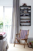 Garden deckchair below toys on wall-mounted shelves and foot of bed in front of French windows