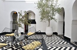 Table and wire shell chairs on black and white tiled floor with zigzag pattern in Moroccan courtyard