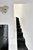 Masonry staircase with black painted runner; wooden door with Moroccan metal fittings and hammered metal dishes on wall