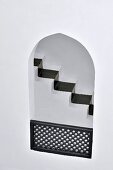 View of black painted runner on narrow staircase through Oriental arched aperture with wooden balustrade