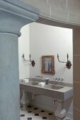 Doorway next to classical stone column with view of modern washstand below antique sconce lamps