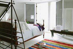 Modern, open-plan sleeping area with antique bed on partially visible striped rug opposite open double terrace doors