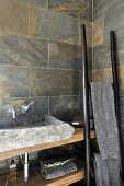 Rustic stone wash basin on wooden counter with ladder-like towel rack leaning on wall in corner of bathroom with marbled stone tiles