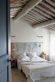 Blick durch Tür auf französisches Bett mit über Stangen gewickelten Pendelleuchten und rustikaler, mediterraner Dachkonstruktion