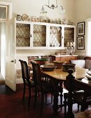 Dining table and antique chairs across from a white, wall mounted display cabinet with lead glass doors