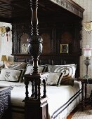 Stack of decorative pillows on a canopy bed with carved posts and colonial style, dark wood canopy