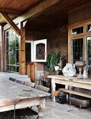 Rustikaler Holztisch mit Stühlen auf überdachter Terrasse vor Landhaus mit Ziegelfassade und Bleiglasfenstern im Jugendstil