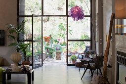 Artistic collection of furniture and objets in loft apartment in front of glass wall with view of greenery on terrace