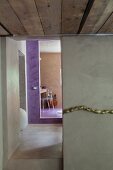 Polished concrete in corridor with violet-painted bathroom entrance at far end; stylised gold cord decorating wall in foreground