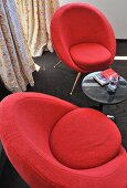 50's look red upholstered chairs and side table on a black carpet in the corner of a room in front of a window with floor to ceiling drapes