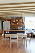 Moderner Essplatz in skandinanvischem Stil vor offener Küche und Frau hinter Küchenblock