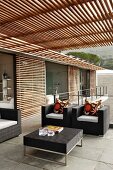 Modern house with elegant, black outdoor furniture on terrace under slatted pergola and with wooden louver blinds on glass wall