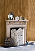 Retro style, fireplace screen with floral pattern and logs in a basket in front of a paper mache fireplace in front of a wall with wood design