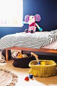 Toys and books in knit baskets in front of a child's bed with stuffed animals