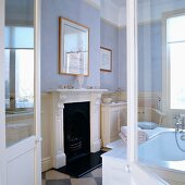 View through open double doors of fireplace with white, carved wooden surround in traditional bathroom with walls painted in pastel shades