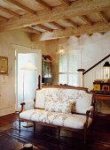 Antique couch with floral upholstery in interior with rustic, wood-beamed ceiling