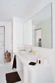 Minimalistisches, weisses Badezimmer mit großem Spiegel über dem Waschtisch, dazu dunkel kontrastierende Handtücher