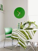 Style mix while dining - modern green chair and white shell chair at a round table with a striped tablecloth in front of a green wall clock in the corner of the room