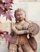 Statue of Oriental goddess; blurred foliage in background
