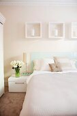 Double bed with bedspread and scatter cushions in pastel, natural shades below white decorative picture frames on wall in delicate cream