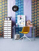 Mixture of boldly patterned wallpapers as backdrop for modern office area with tall, neutral-coloured set of drawers, plexiglass table and swivel chair