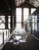 Tischreihe mit Ghoststühlen auf Galerie in einer ehemaligen umgenutzten Fabrikhalle
