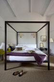 Black, designer four-poster bed and ladies' shoes on sisal carpet in converted attic hotel room