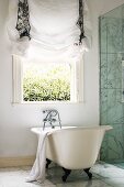 Free-standing bathtub below open window with gathered drape