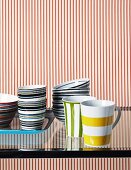 Colourful crockery on glass table in front of red and white striped wall