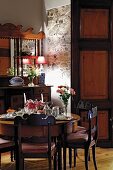 Place settings on round Biedermeier table and antique cabinet with mirrored top in dining room
