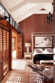 Elegant bedroom in light and dark natural shades; glass wall on one side with slatted shutters