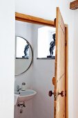 View through open wooden door into bathroom with sink below round mirror