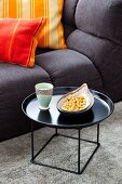 Snacks on black side table and comfortable sofa with striped scatter cushions