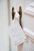 Karte mit geschriebenem Gruss an Vintage Türknauf einer weissen Zimmertür hängend