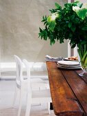 weiße Stühle vor rustikalem Holztisch mit Blumenvase