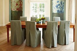 Chairs with simple, light gray covers at a long wooden table in a modern dining room with traditional flair