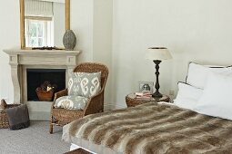 Animal skin bedspread on a double bead and rattan chair in front of an open, classic fireplace in a bedroom with traditional flair
