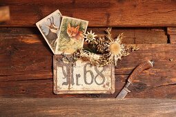 Karten mit Tierzeichnungen und Silberdistel über Hausnummer neben Hornmesser an Hüttenwand befestigt