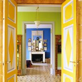 Open, colourfully painted double doors and view through green anteroom into blue interior with open fireplace