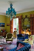 Traditioneller, englischer Wohnraum mit starken Farbkontrasten durch gelb gemusterte Tapete, rote Chintz Vorhänge, blauem Sofa und türkisblauem Kronleuchter