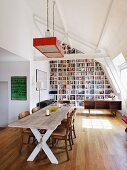 Dachraum mit imposanter Bücherwand, einer rustikalen Esstafel und eleganten Stühlen mit Ledersitzen