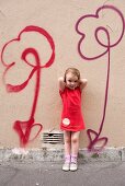 Kleines Mädchen steht vor einer mit Blumen besprühten Wand