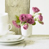 Pink roses in ceramic vase, teacups and side plates
